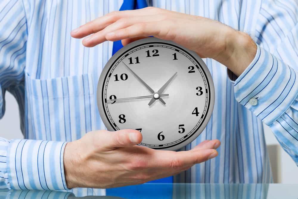 businessperson holding analog clock with two hands indicating patient appointments