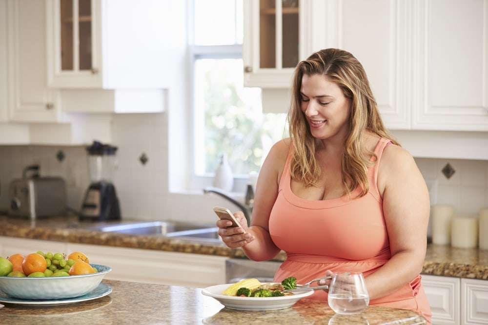 woman in kitchen holding smartphone to engage with doctor's office using dash chat
