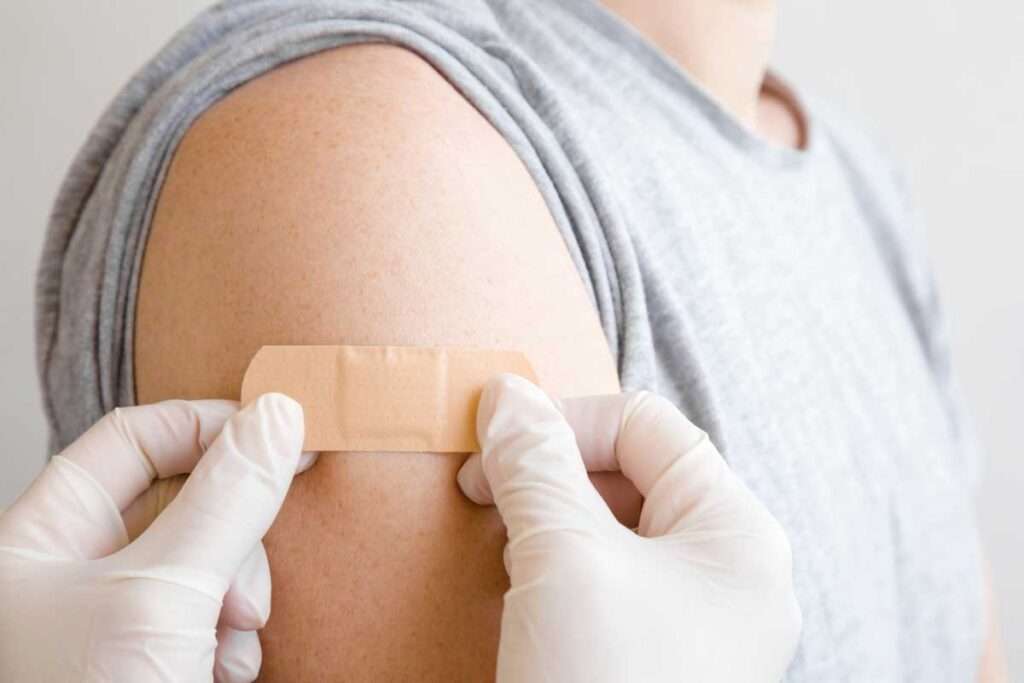 gloved hands applying bandaid to patient's arm