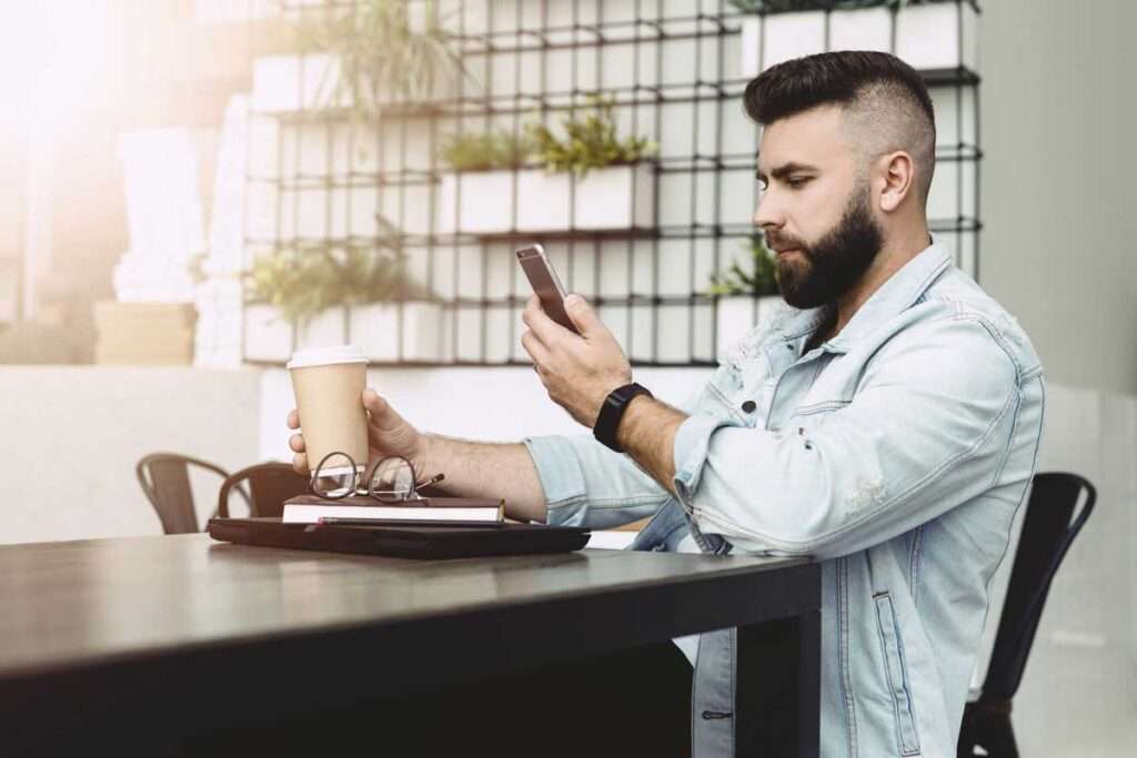 man holding coffee and using smart phone to set doctor appointment online