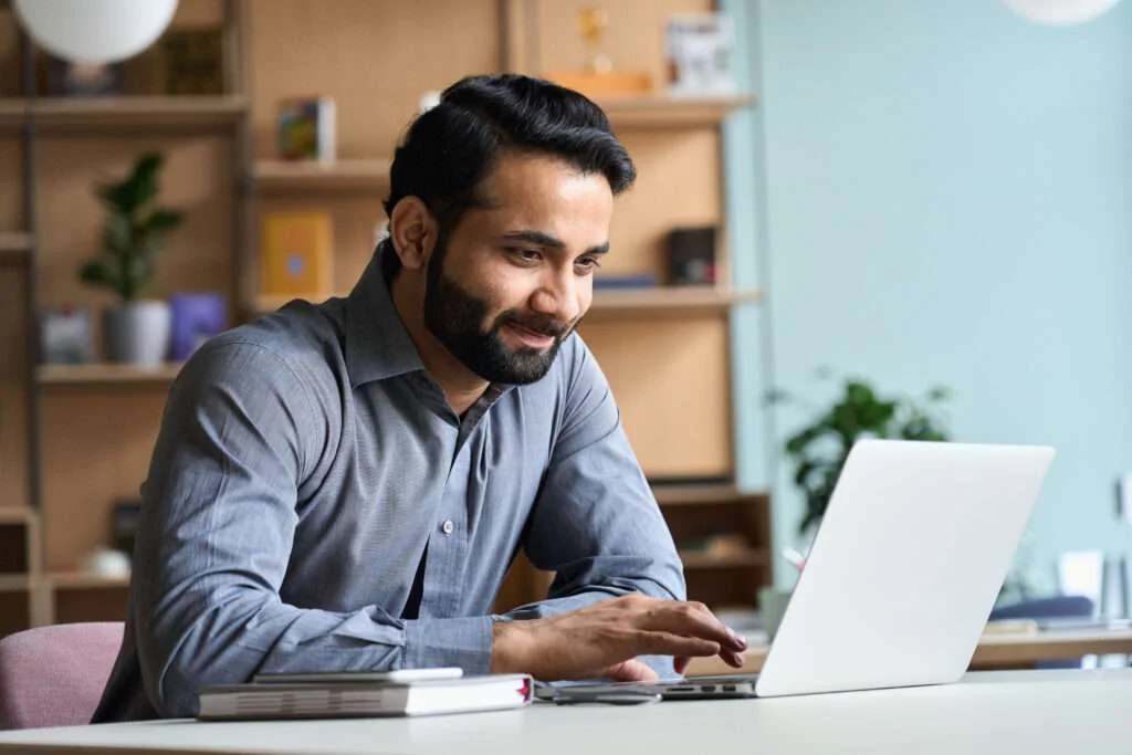 Smiling business man using patient intake management software on laptop computer at home office.